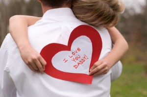 Little girl holding father's day card and hugging dad.