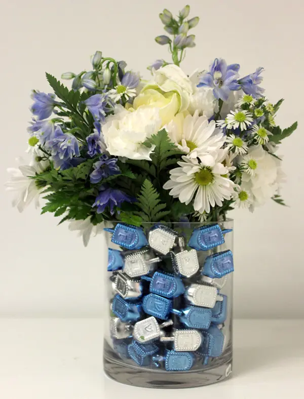 DIY Hanukkah centerpiece with dreidels and flowers in a vase.
