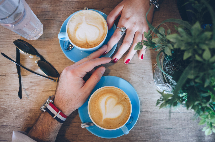 Rainy day date ideas with two cups of coffee and two hands touching on a table.