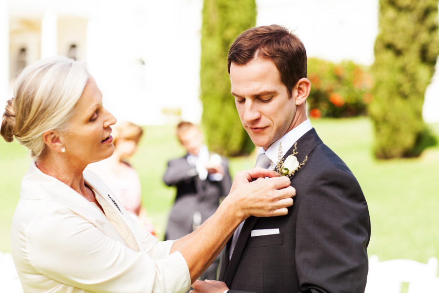 mother pinning boutonniere on son at wedding