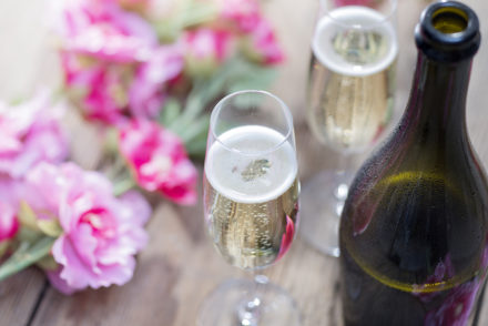 Bottle of Prosecco and two champagne glasses on a rustic garden picnic table with blossom or flowers in the background. Springtime or Summertime.