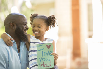 Little girl gives homemade card to her dad in front yard of family home.