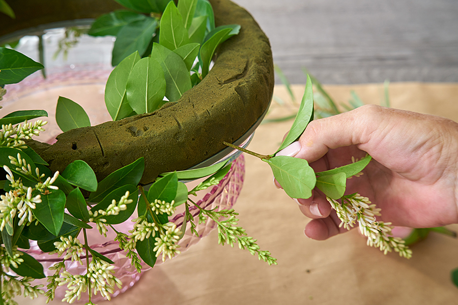 a photo of a roses and rosé wreath with pushing leaves into floral foam