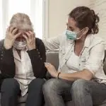 Woman wearing mask comforting older woman