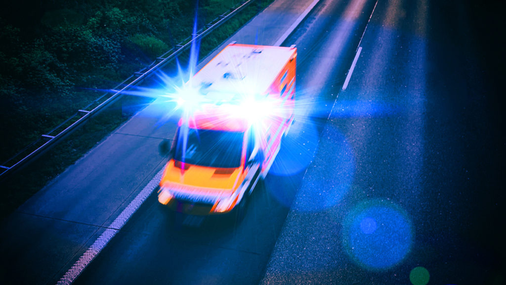 An ambulance drives with lights flashing on a highway
