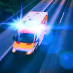An ambulance drives with lights flashing on a highway