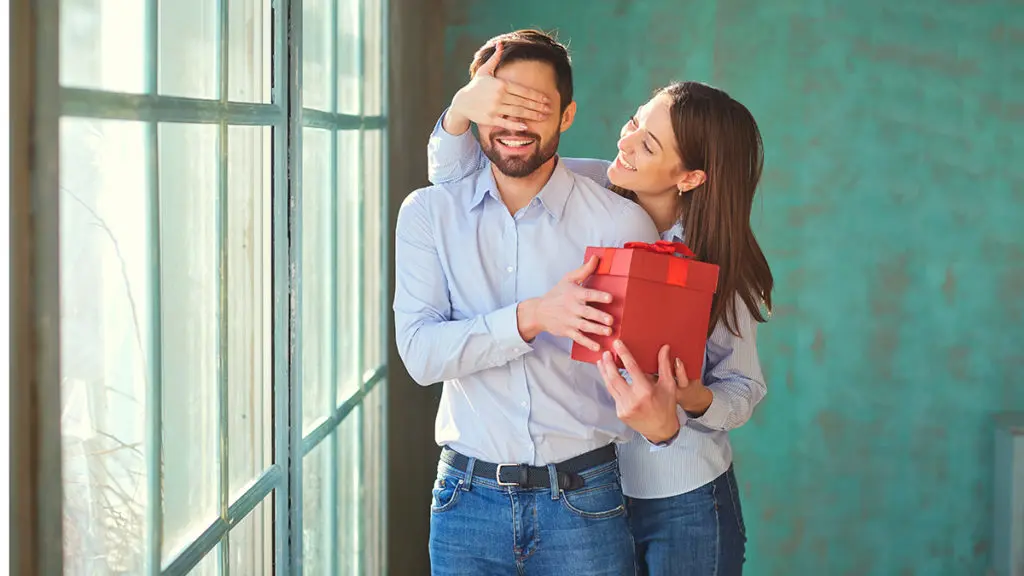 Valentine’s Day Gift Guide with Woman surprising man with gift in red box