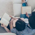 Top view portrait of well-read lettered couple enjoying reading novel poem, poetry fans, lying on sofa having books in hands. Hobby free time self-development education concept