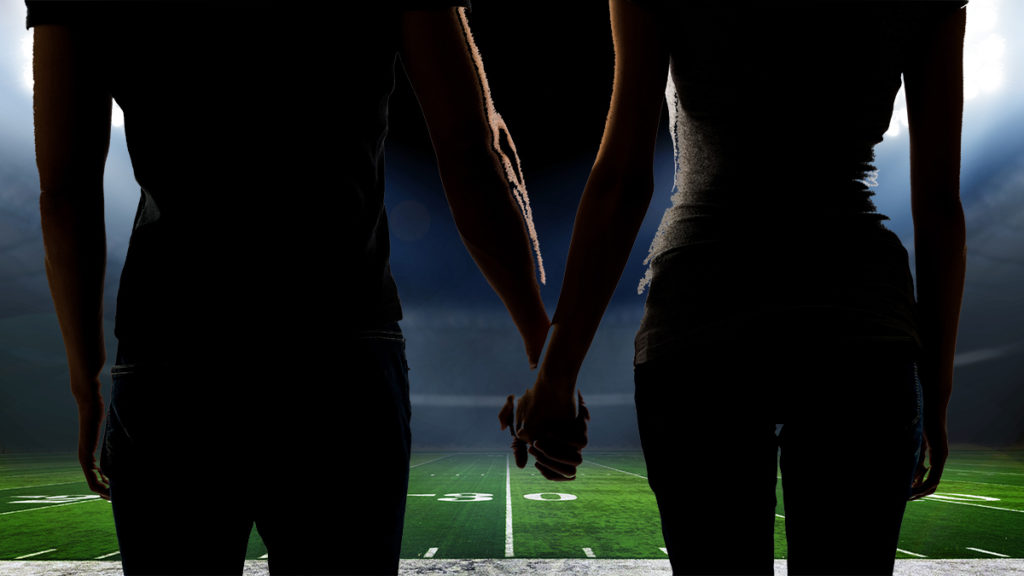 A couple holds hands on the 50-yard line of an American football stadium