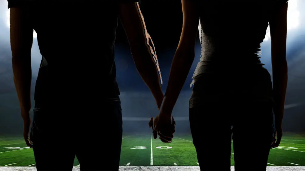 A couple holds hands on the 50-yard line of an American football stadium