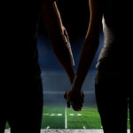 A couple holds hands on the 50-yard line of an American football stadium