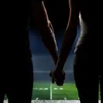 A couple holds hands on the 50-yard line of an American football stadium