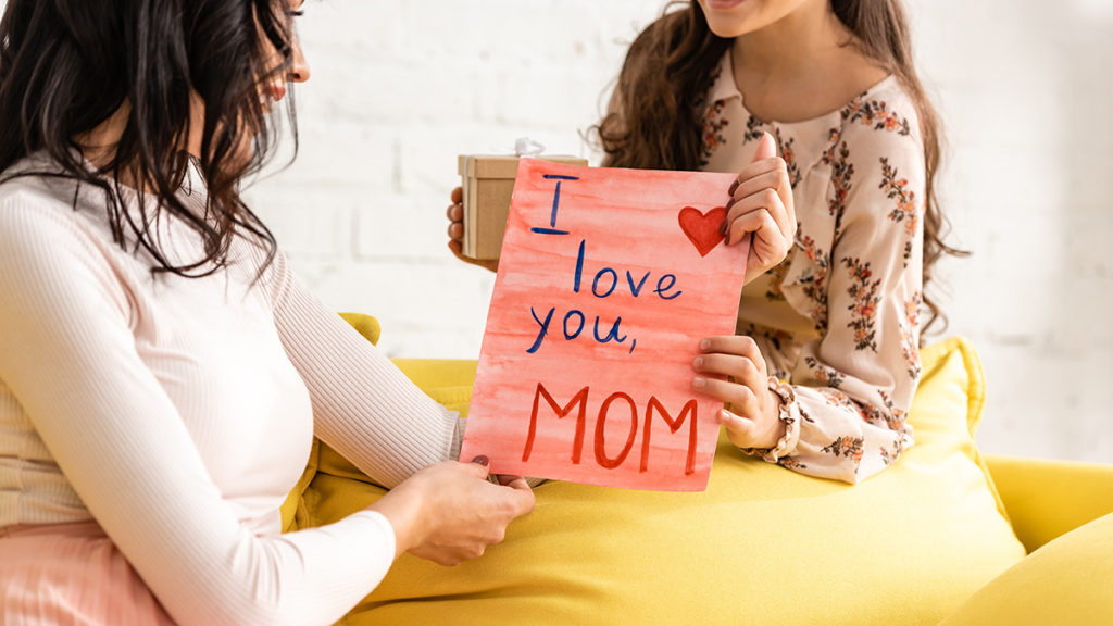 a photo of mother's day: daughter giving mom an "I love you, Mom" sign