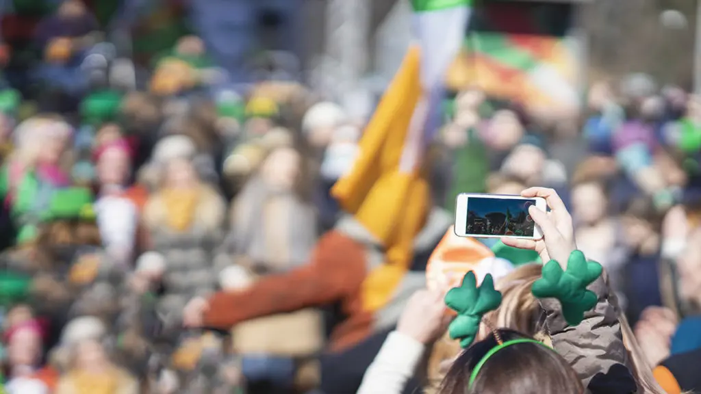 A photo of a woman holding a smartphone while celebrating St. Patrick's Day