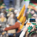 A photo of a woman holding a smartphone while celebrating St. Patrick's Day