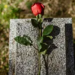 A photo of a rose against a headstone at a cemetery.