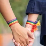 Two women holding hands adorned with rainbow bracelets