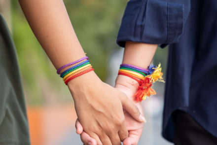 Two women holding hands adorned with rainbow bracelets