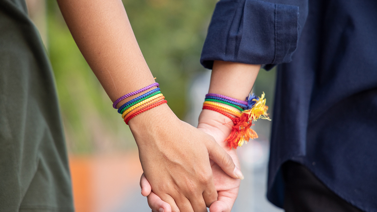 Two women holding hands adorned with rainbow bracelets