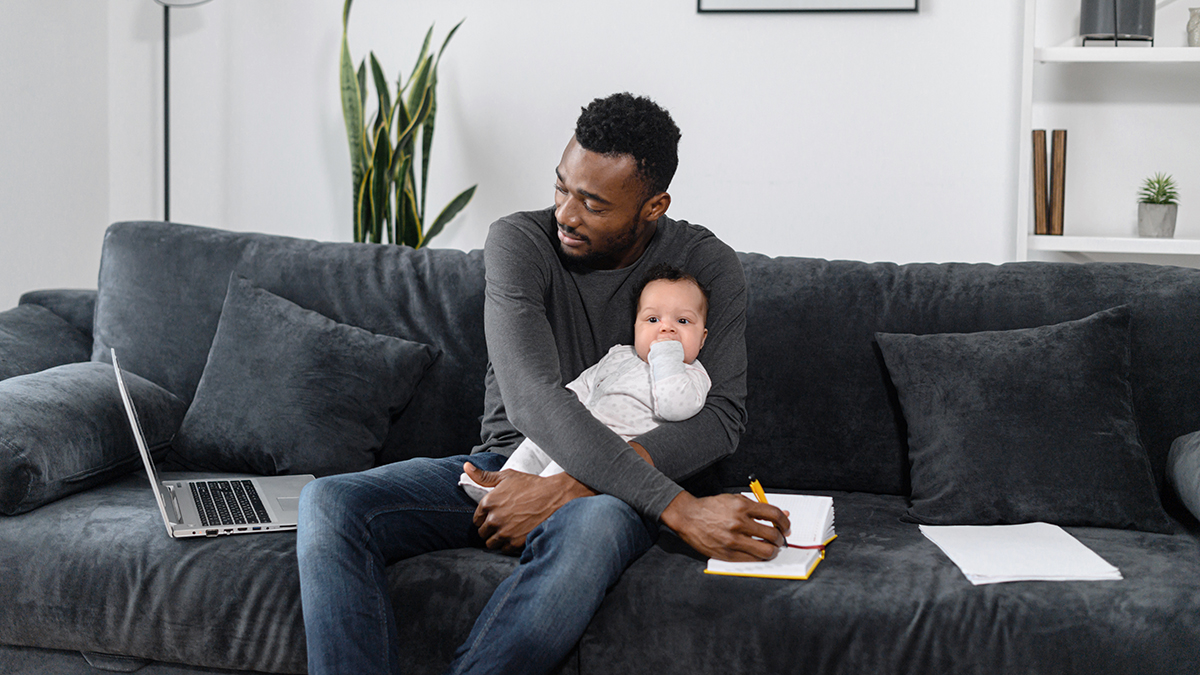 This is an image of daddy brain while a dad is working from home holding his infant child. 