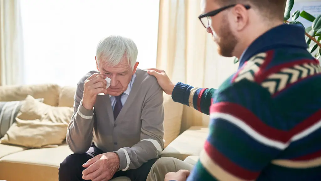 Photo of empathetic psychologist consoling man and stroking his shoulder while supporting him and cheering up during therapy session