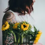 Photo of a woman holding sunflowers next to her flower tattoo