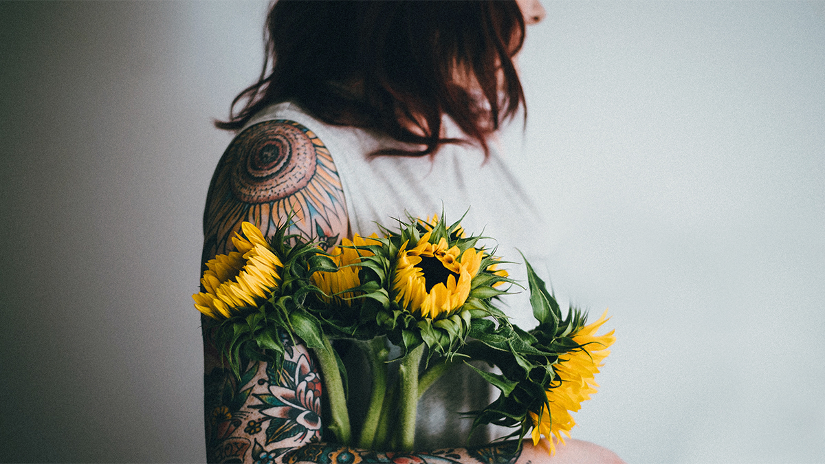Foto de una mujer sosteniendo girasoles junto a su tatuaje floral