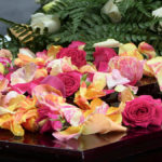 Floral arrangements for a funeral should be colorful and joyful. This photo shows yellow and red flowers atop a casket.