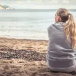 importance of remembrance with young woman remembering a lost loved one while sitting alone at the seashore