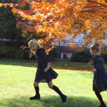A photo of two girls playing amid autumnal trees and loving fall.