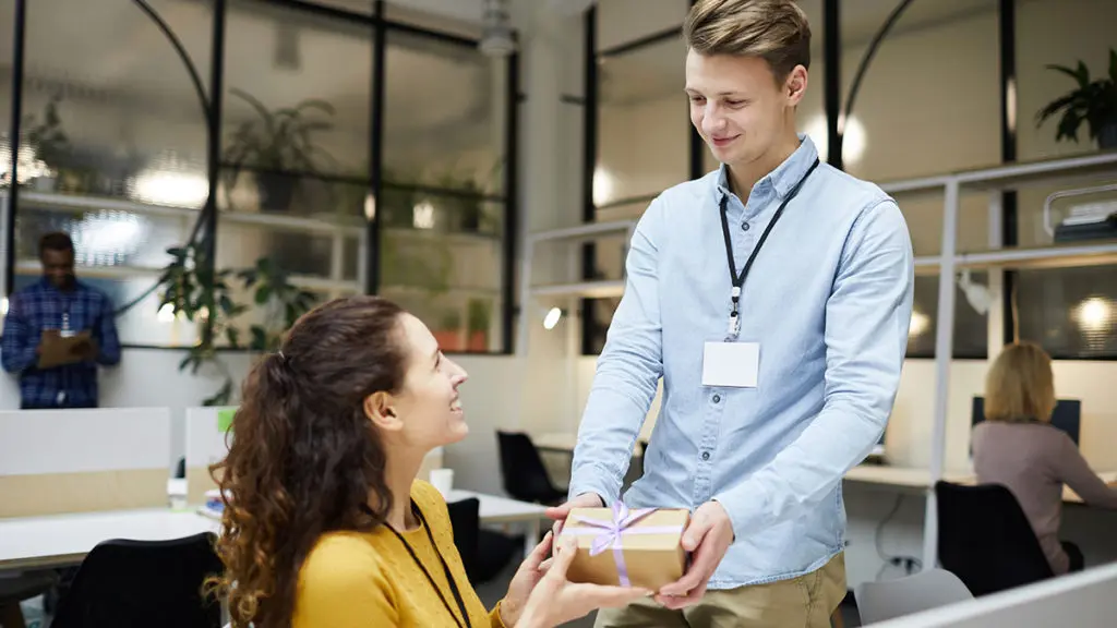 Photo of a young manager delivering a gift to her employee as part of their company's corporate gifting program