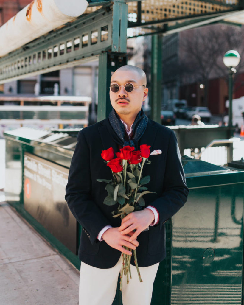 Date night ideas for men with a man holding a bouquet of roses standing next to a subway station.