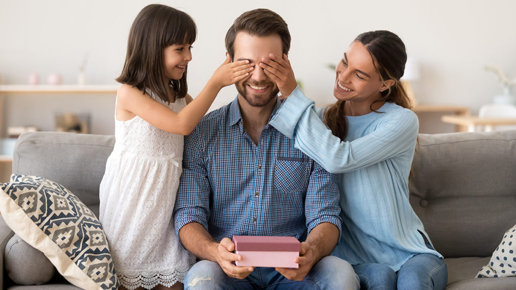 Una foto de mensajes del día del padre con esposa e hija dando un regalo del día del padre a papá