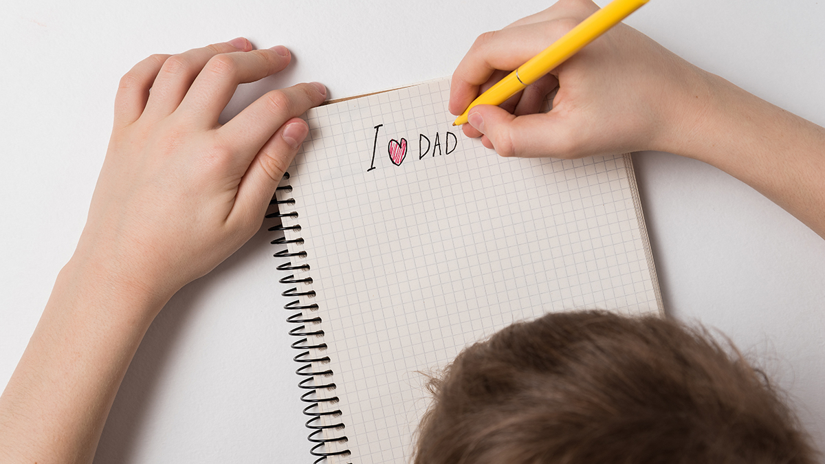 Una foto de mensajes del día del padre con un hijo escribiendo una nota del día del padre para papá