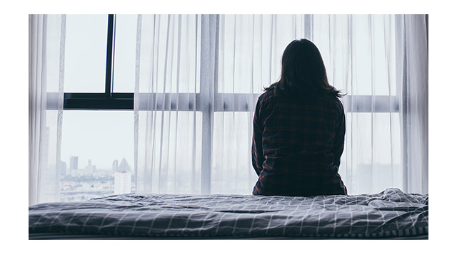 Photo of a woman sitting on the bed while struggling with mental health challenges