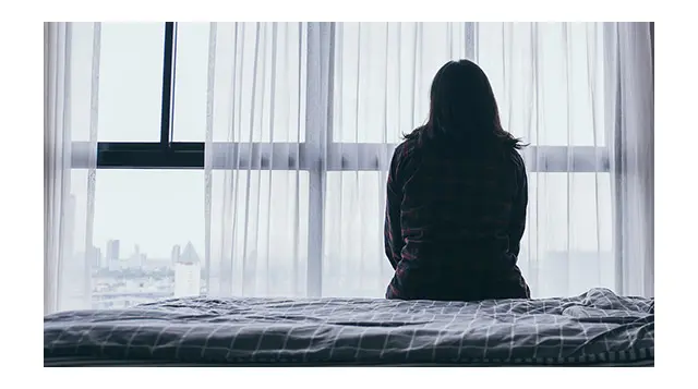 Photo of a woman sitting on the bed while struggling with mental health challenges