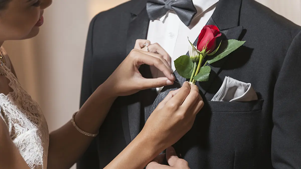 a photo of corsage and boutonniere with a woman pinning a boutonniere on her prom date's lapel