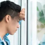 a photo of collective grief with a man leaning on window looking worried