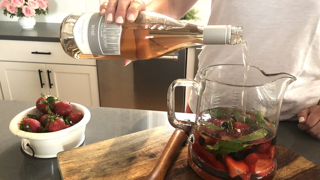 Photo of rosé sangria with pouring a bottle of rosé into a pitcher of fruit