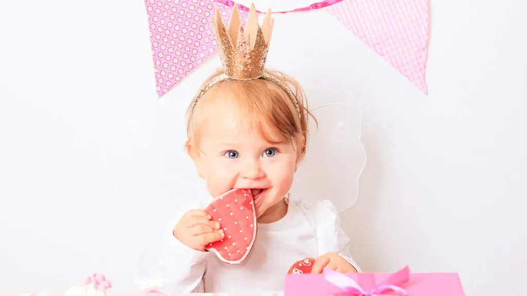 a photo of first birthday party tips with a baby eating a heart-shaped cookie