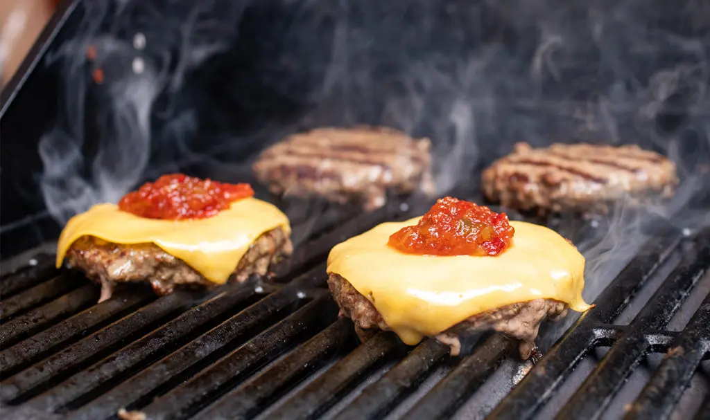 a photo of grill burgers with cheeseburgers on the grill wit ketchup and relish
