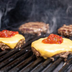 a photo of grill burgers with cheeseburgers on the grill wit ketchup and relish