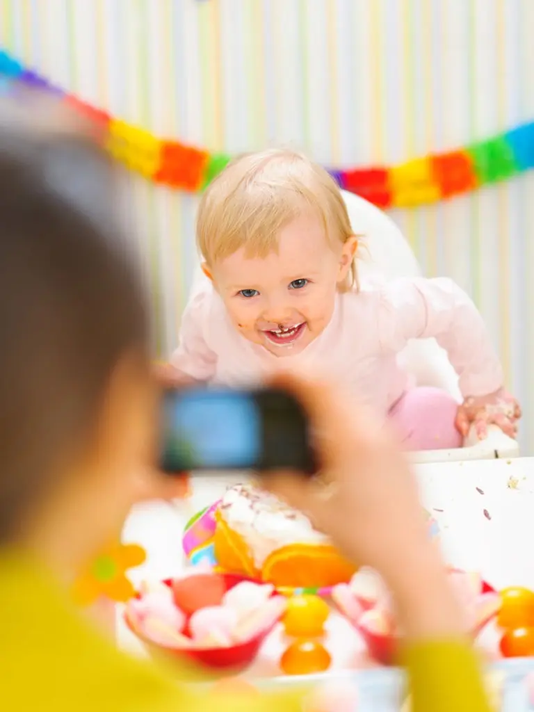 a photo of first birthday party tips with a mom taking a picture of her baby eating cake