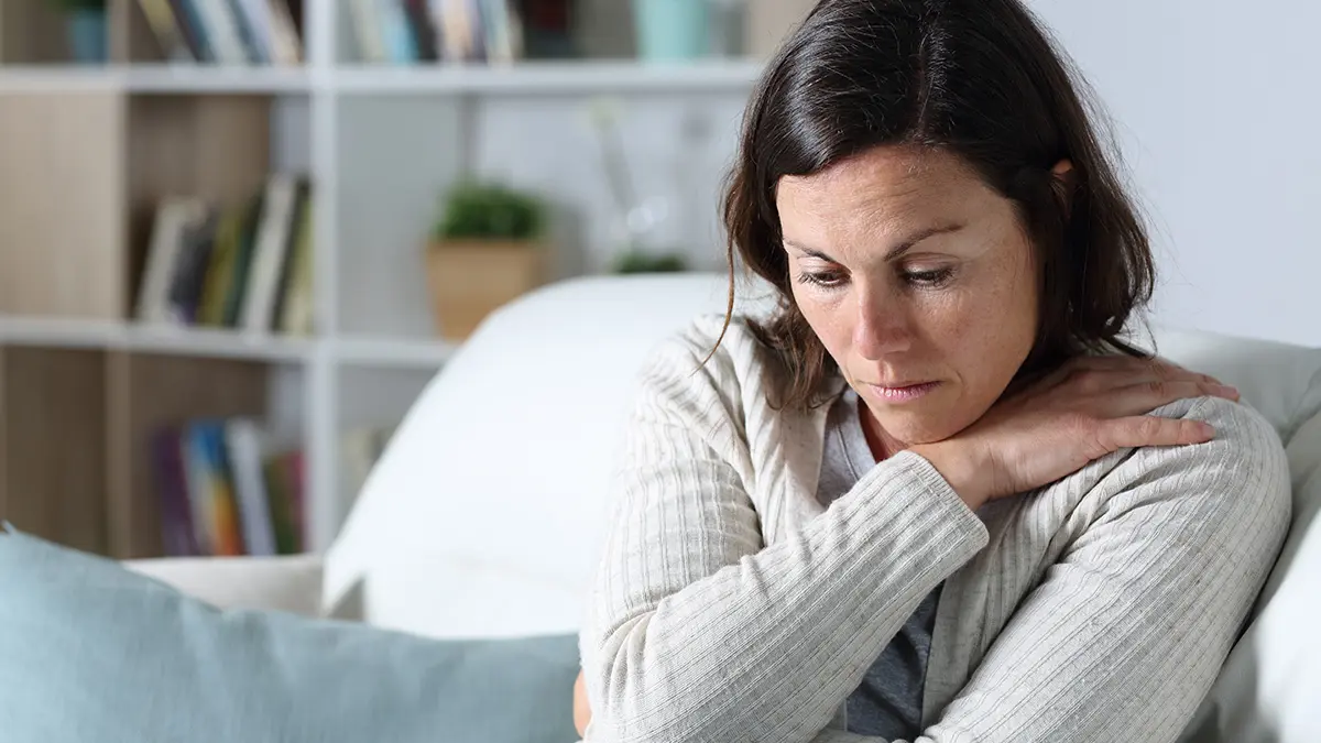 how to write an obituary with a pensive-looking woman sitting at home on her couch