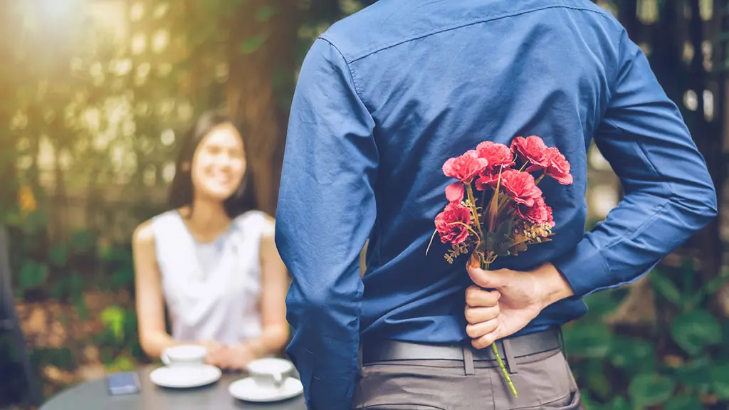 Photo of flowers for a date with a man hiding red flowers behind him in order to surprise his girlfriend