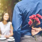 Photo of flowers for a date with a man hiding red flowers behind him in order to surprise his girlfriend