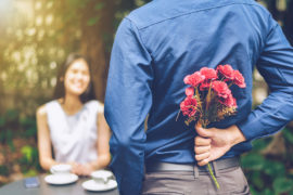 Photo of flowers for a date with a man hiding red flowers behind him in order to surprise his girlfriend
