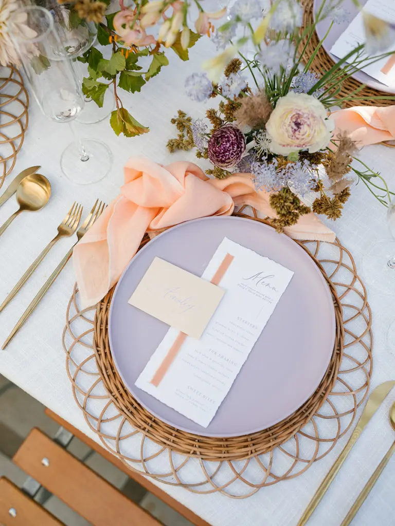 Bridal shower table setting with menu, flowers, glasses and utensils.