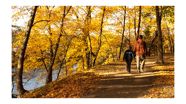 A father and son are celebrating fall by walking down a biking path