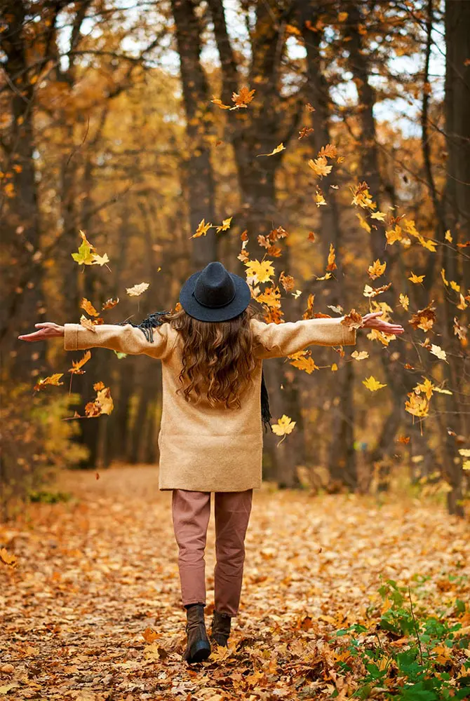 Happy excited young woman under leaves fall